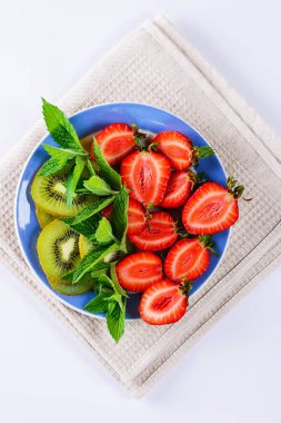 Dilimlenmiş çilek, kivi meyve ve nane yaprakları bir tabakta. Meyve salatası.