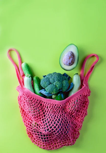 String bag with green vegetables on a light green background. Zero waste concept, flat lay, copy space.