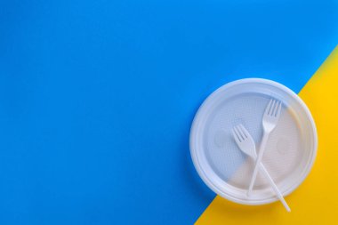 Mavi ve sarı arka planda beyaz plastik tabaklar. Düz yatıyordu, horisontal oryantasyon, kopyalama alanı.