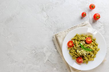 Gri bir arka plan üzerinde fesleğen, domates ve peynir ile Pesto makarna. İtalyan geleneksel mutfağı. Düz döşeme, kopyalama alanı.
