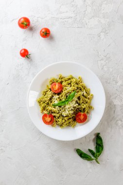 Gri bir arka plan üzerinde fesleğen, domates ve peynir ile Pesto makarna. İtalyan geleneksel mutfağı. 