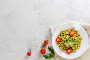 Gri bir arka plan üzerinde fesleğen, domates ve peynir ile Pesto makarna. İtalyan geleneksel mutfağı. Düz döşeme, kopyalama alanı.