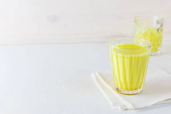 Golden milk from turmeric, vegetable milk, pepper, ginger, coconut oil, maple syrup in a glass on a white background. Traditional indian drink, copy space.
