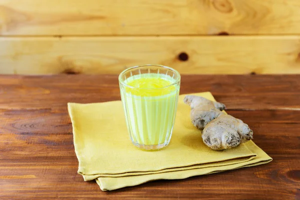 Golden milk from turmeric, vegetable milk, pepper, ginger, coconut oil, maple syrup in a glass on a wooden table. Traditional indian drink, copy space.