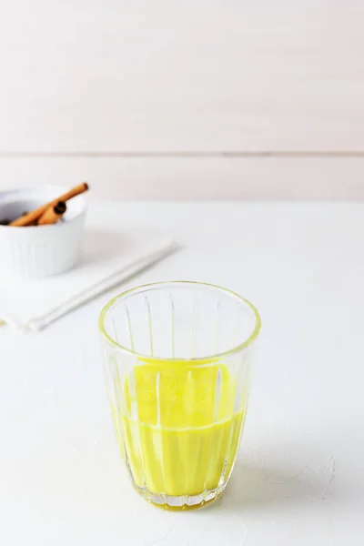 Golden milk from turmeric, vegetable milk, pepper, ginger, coconut oil, maple syrup in a glass on a white background. Traditional indian drink.