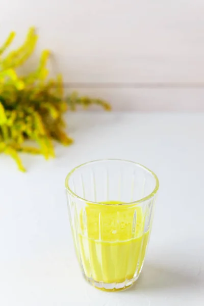 Golden milk from turmeric, vegetable milk, pepper, ginger, coconut oil, maple syrup in a glass on a white background. Traditional indian drink.