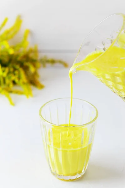 Golden milk from turmeric, vegetable milk, pepper, ginger, coconut oil, maple syrup in a glass on a white background. Traditional indian drink.
