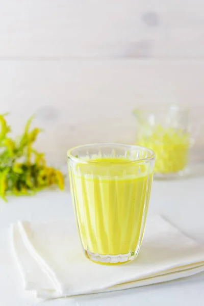 Golden milk from turmeric, vegetable milk, pepper, ginger, coconut oil, maple syrup in a glass on a white background. Traditional indian drink.