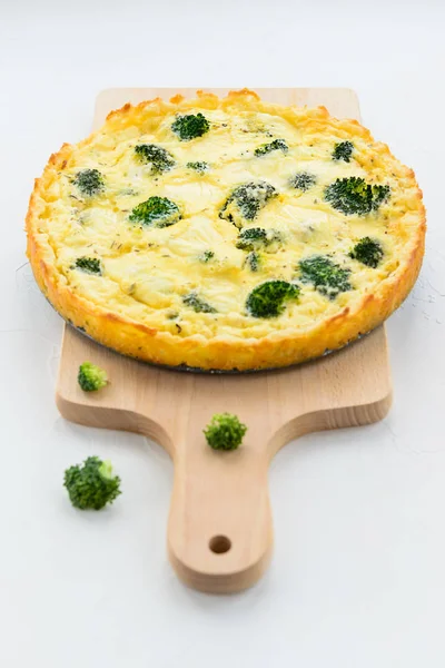 Homemade tart with broccoli and cheese on a white table.