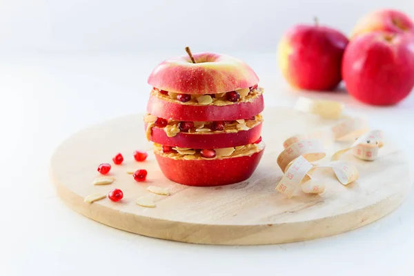Apple vegetarian burger with nut paste, pomegranate seeds, almonds and measuring tape on a wooden board. Proper nutrition concept.