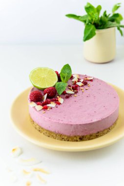 Beyaz arka planda ahududu, nane ve limonlu soğuk çiğ kaju keki. Vejetaryen tatlı, şekersiz, glüten, laktoz.