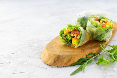 Tahta bir tahtanın üzerinde sebzeli rulo, somon ve pirinç kağıdında otlar. Yatay yönelim, boşluğu kopyala.