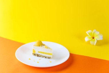 Sarı-turuncu arka planda mango marmelatlı çiğ kaju keki ve frangipani çiçeği. Şeker, laktoz, glütensiz.