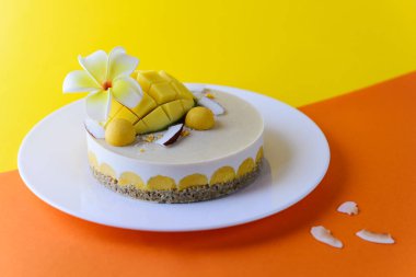 Mangolu kaju keki, hindistan cevizi ve sarı-turuncu arka planda frangipani çiçeği. Şeker, laktoz, glütensiz. Sağlıklı yemek, vejetaryen..