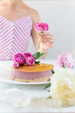 Portakallı ve kirazlı kremalı kaju keki. Bir kadın bunu güllerle süslüyor. Şeker, laktoz, glütensiz. Sağlıklı yemek, vejetaryen..