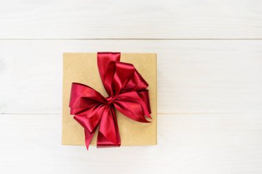 Hafif ahşap arka planda kırmızı fiyonklu bir hediye kutusu. Yatay yönelim, boşluğu kopyala.