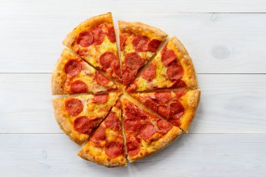 Beyaz ahşap bir masada dilimlenmiş pepperoni pizza..