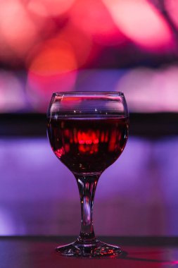 kırmızı bir içki ile bir cam kadeh bulanık bir arka planda masada duruyor