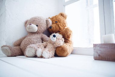 Kızıl saçlı ve iki bej oyuncak ayı beyaz bir pencere üzerinde oturuyor