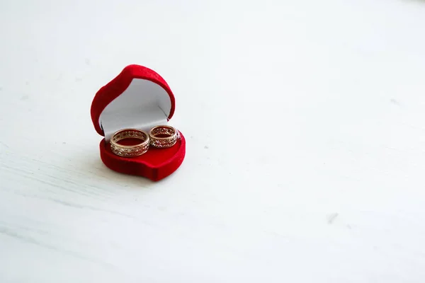 The red box in the form of a heart is open on a white steel. In it are two wedding gold carved rings.