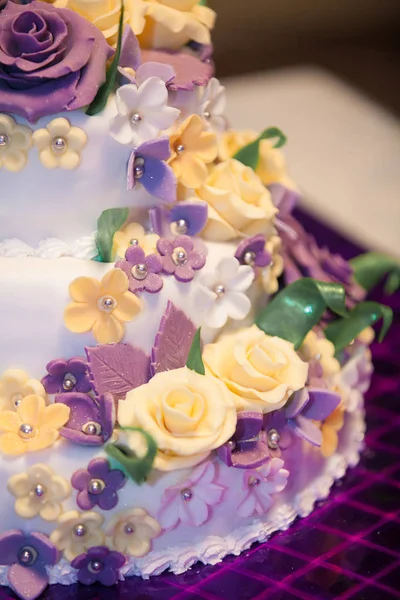 Yellow and purple flowers on a white wedding cake with green leaves