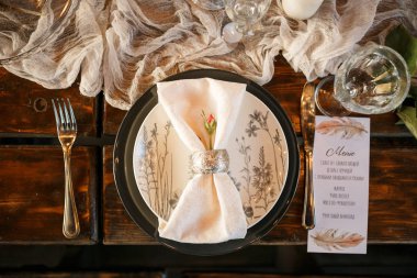 Ahşap bir masa üzerinde siyah bir tabak, üzerinde bir çiçek deseni ve bir gül tomurcuk ile gümüş bir yüzük bir peçete ile beyaz. Sağtarafta bir bıçak ve menü lü bir kart var; Bir kadeh şarap bardağı var. Kartpostalda taze sebze salatası yazıyor, Sezar.