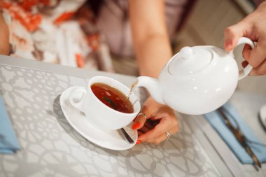 Beyaz bir fincan bir tabak üzerinde duruyor. Su ısıtıcısından siyah çay dökülür..