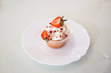 Beyaz bir tabak üzerinde açık krema, çikolata cipsi ve yeşil yaprakları ile kırmızı çilek yarısı ile oluklu sarıcı bir muffin yatıyor. yatay çerçeve.