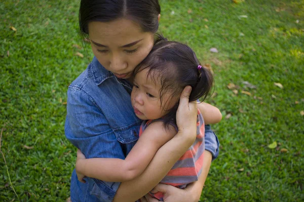 Young mother hugging and soothing a crying little daughter, Asia