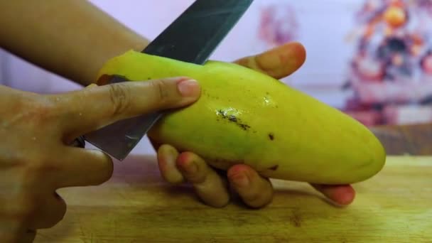 Jonge vrouw reinigt en snijdt mango. Meisje peeling mango en houd het in de hand, cuting door mes. peeling rijpe mango, rijpe mango en het paring mes dat wordt gebruikt om te schillen is op de achtergrond. — Stockvideo