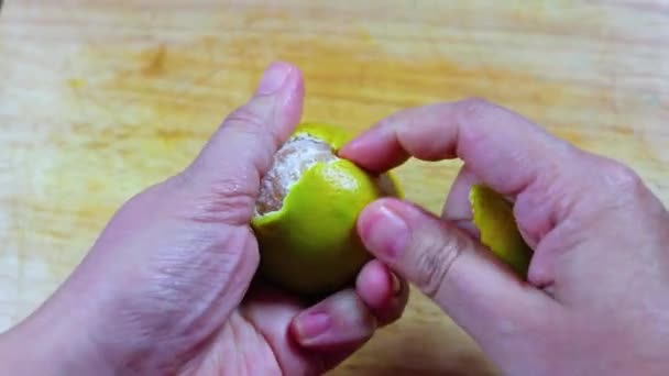 Girl peeling orange and hold it in hand,  close up over wooden cutting board. — Stock Video