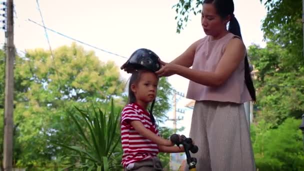 Мати допомагає своєму синові (хлопчику з довгим волоссям) одягати велосипедний шолом на відкритому повітрі . — стокове відео