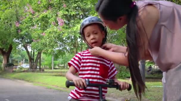 Mère aidant son fils (garçon aux cheveux longs) à mettre un casque de vélo à l'extérieur . — Video