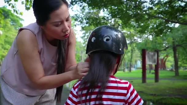 Moeder helpt haar zoon (lang haar jongen) om te zetten op fietshelm buitenshuis. — Stockvideo