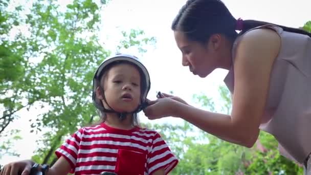 Mutter hilft ihrem Sohn (Langhaarjunge), im Freien einen Fahrradhelm aufzusetzen. — Stockvideo