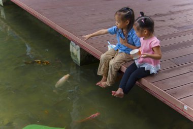 Küçük çocuklar suya bakar lar ve tahta br'de balıkları beslerler.