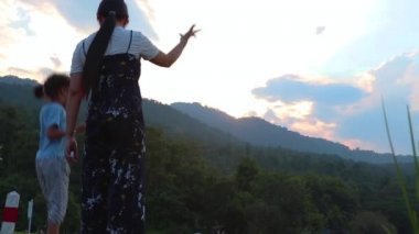 Annem çocukları geride bırakıp gün batımında göle bakıyor. Doğada, tatilde, açık havada genç bir ailenin portresi. Aile tatili kavramı.