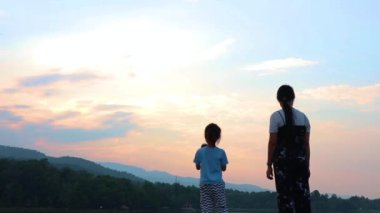 Annem çocukları geride bırakıp gün batımında göle bakıyor. Doğada, tatilde, açık havada genç bir ailenin portresi. Aile tatili kavramı.
