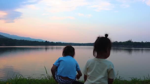 Niños felices niño y niña hermano y hermana juegan juntos se quedan atrás y mirando el lago al atardecer . — Vídeo de stock
