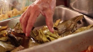 Elinde muz yaprağında köri ezmeli Tayland Balığı tutan bir sokak satıcısı..