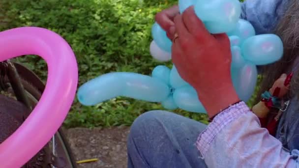 Klaun na volné noze, který vytváří balónová zvířata a různé tvary na venkovním festivalu v centru města. Školní taška, andělská křídla, motýli a psi z balónků. Koncept zábavy, narozeniny — Stock video