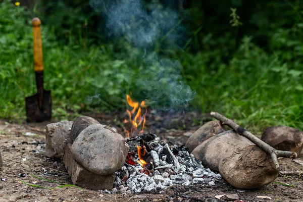 The sharp used shovel spade is stuck in the ground with grass near a campfire