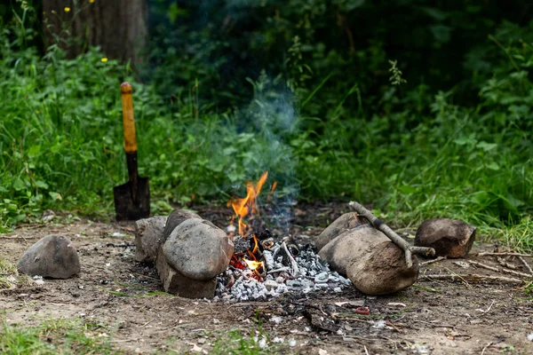 Keskin kullanılan kürek maça bir kamp ateşi yakınında çim ile yere sıkışmış 
