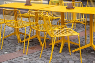 Yağmurdan sonra bir kafede sarı masalar ve sandalyeler.