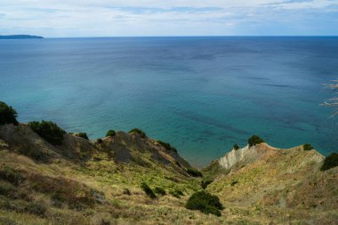 Yunanistan 'ın Korfu adasındaki bir uçurumdan manzara. Parça bulutlu bir gökyüzünün altında turkuaz İyon Denizi 'ne inen yeşil bitki örtüsü olan Rocky sahili. Yaz Akdeniz manzarası, seyahat