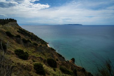 Yunanistan 'ın Korfu adasındaki bir uçurumdan manzara. Parça bulutlu bir gökyüzünün altında turkuaz İyon Denizi 'ne inen yeşil bitki örtüsü olan Rocky sahili. Yaz Akdeniz manzarası, seyahat
