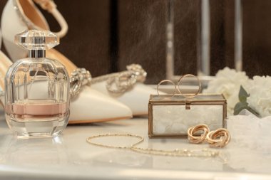 Düğün aksesuarları yüzükler, ayakkabılar ve parfüm bir masada.