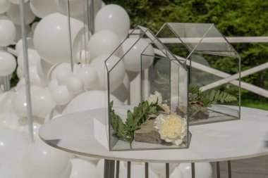 Flower arrangement in the glass box on the table with white balloons
