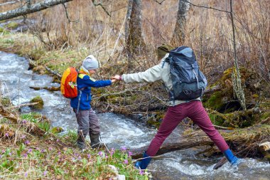 Yürüyüş anne oğlunu dağ dere geçmeye yardımcı olur, elini tutar. Spor ailesi ile sırt çantaları