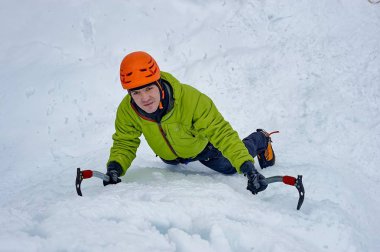 Elinde buz aletleri olan dağcı adam turuncu kasklı baltayla büyük bir buz duvarına tırmanıyor. Açık hava Spor Portresi